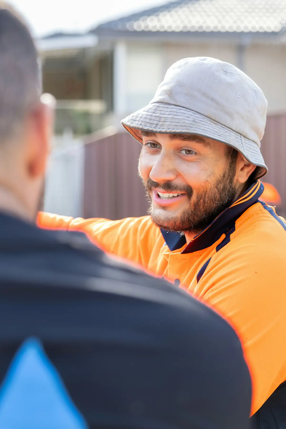 Un artisan souriant échange avec une personne de dos, en extérieur.